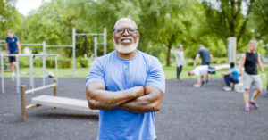 A buff middle-aged black man standing and smiling in front of an outdoor gym.
