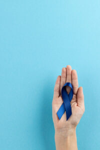 A hand holding a dark blue colon cancer awareness ribbon in it's palm.