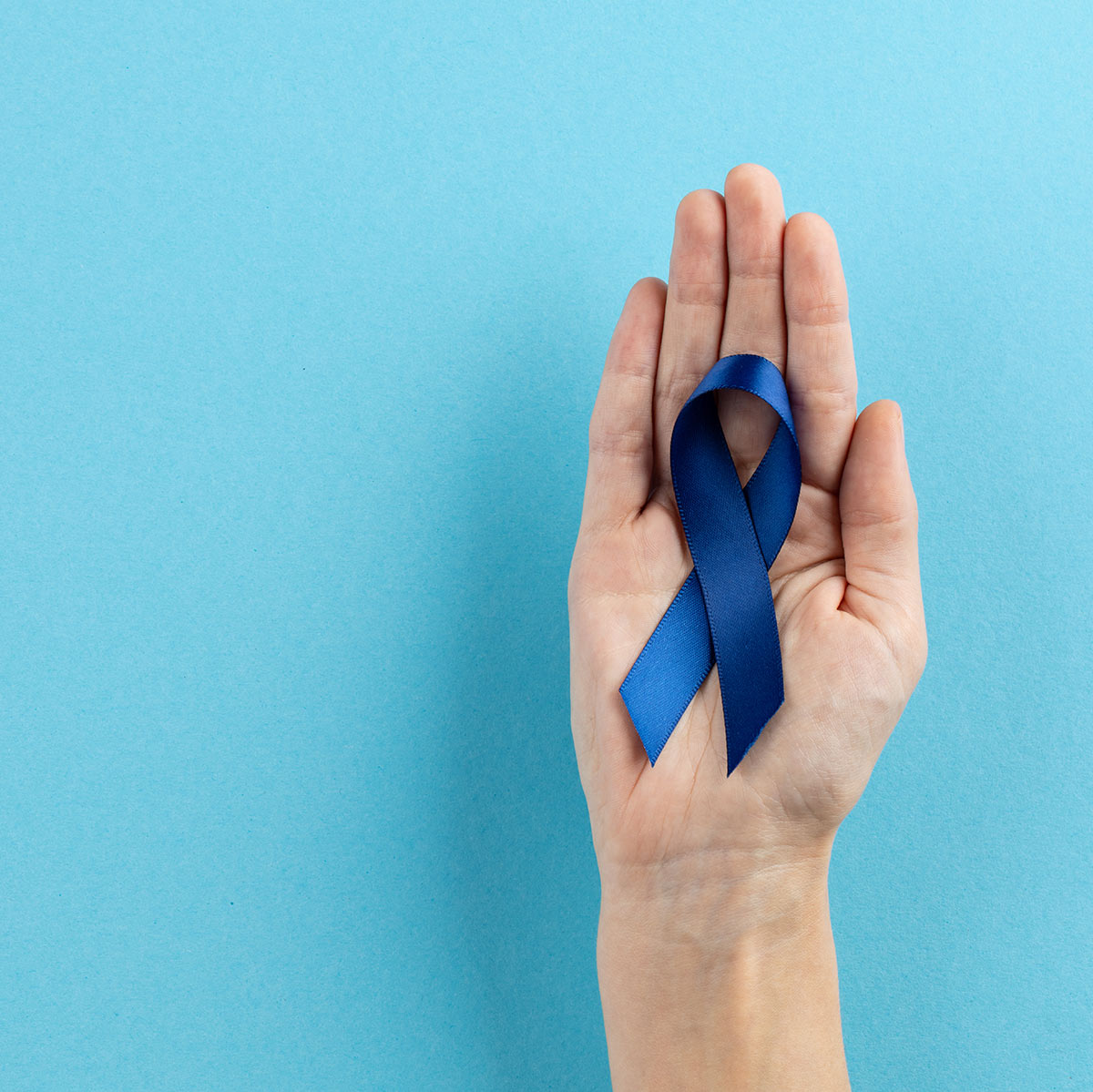 A hand holding a dark blue colon cancer awareness ribbon in it's palm.