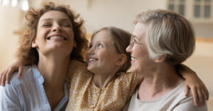 3 generations women. Overjoyed happy little girl embrace shoulders of laughing mother smiling older grandmother. Loving family of three diverse age females spend time together hug on sofa having fun