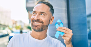 Middle age handsome man smiling happy holding blue prostate cancer ribbon at the city.
