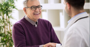 A smiling old man shaking hands with a doctor.