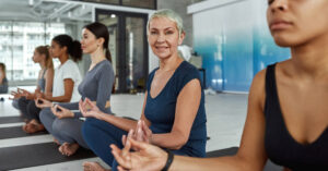 Smiling active middle-aged woman meditate at group training